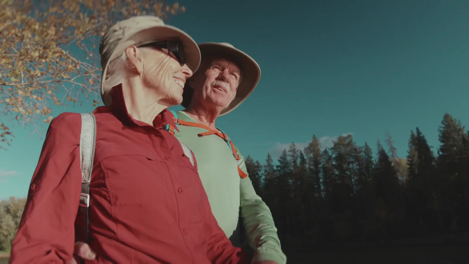 An older couple laughing together outdoors, mountains behind them