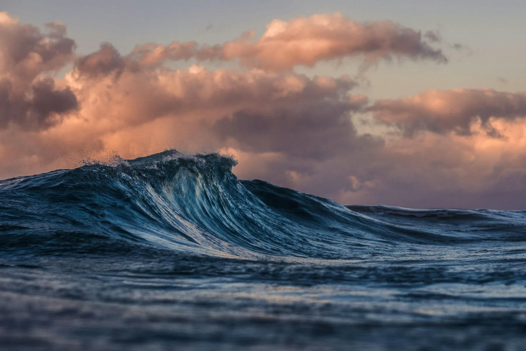 A wave breaking on open ocean under a sunset sky